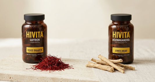 Saffron threads and dried ashwagandha root beside two amber Hivita glass supplement bottles on a stone surface.